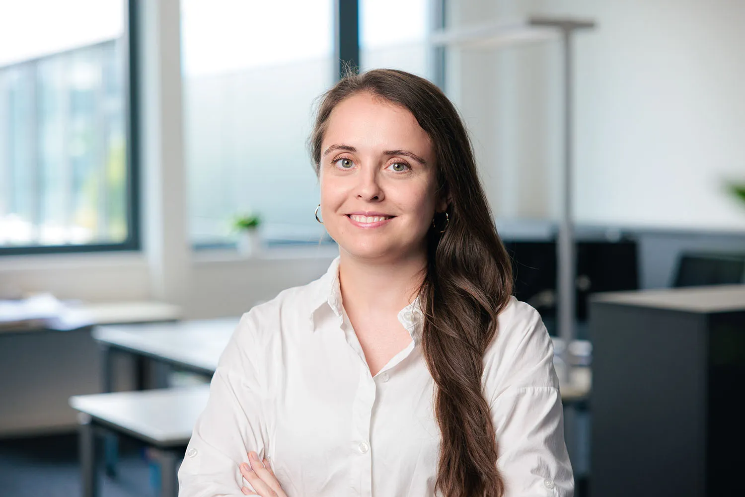 Porträt einer Frau mit langen dunklen Haaren und weißer Bluse, lächelnd im Büro.
