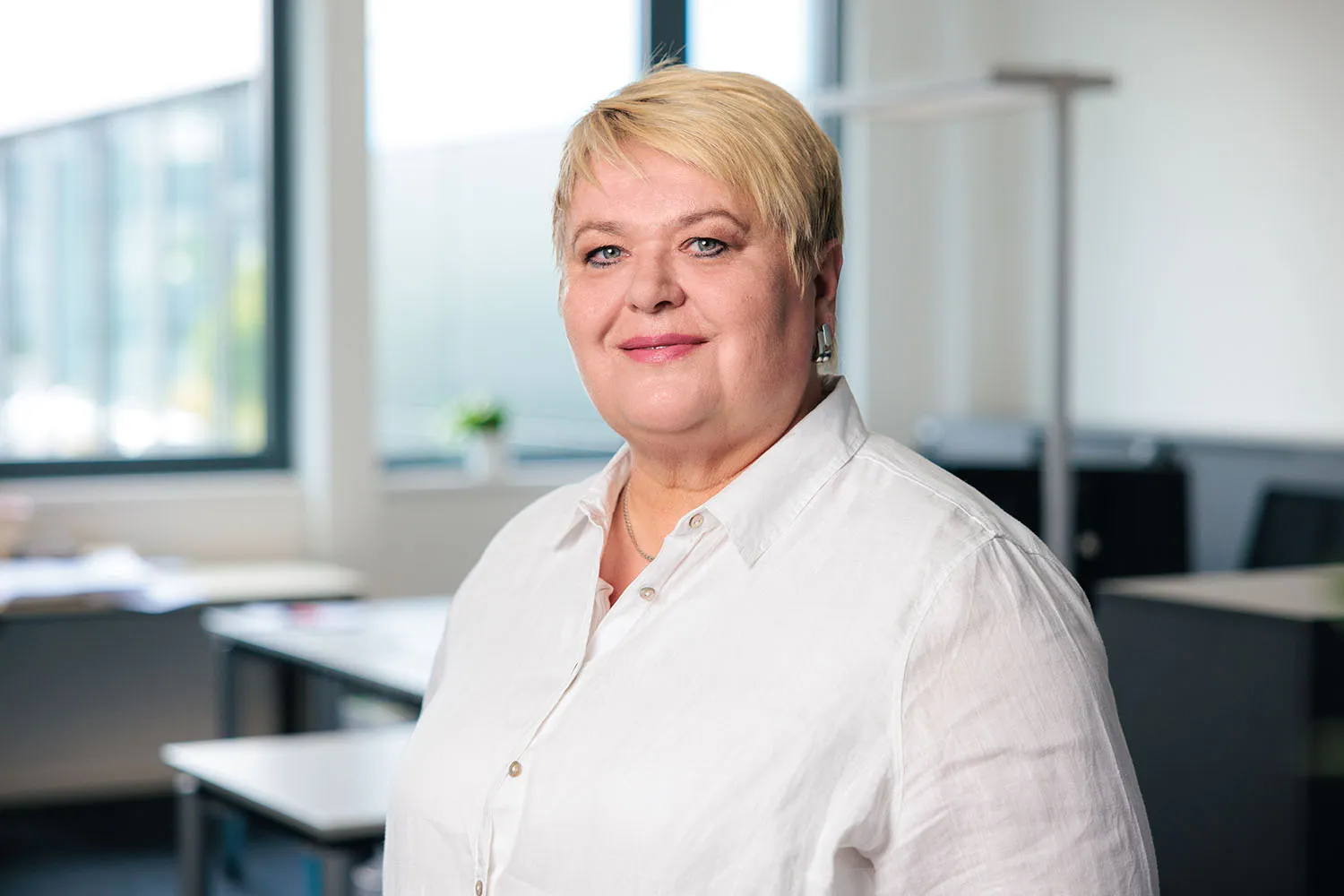 Porträt einer Frau mit kurzem blondem Haar und weißer Bluse vor hellem Büro.