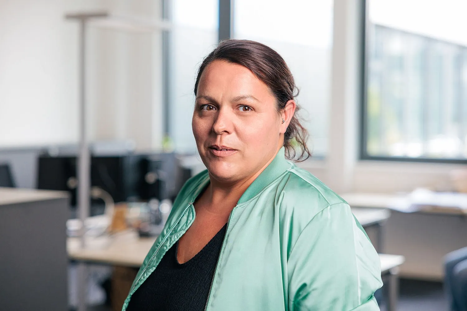 Porträt einer Frau mit dunklen Haaren, grünem Blazer und ernstem Gesichtsausdruck im Büro.