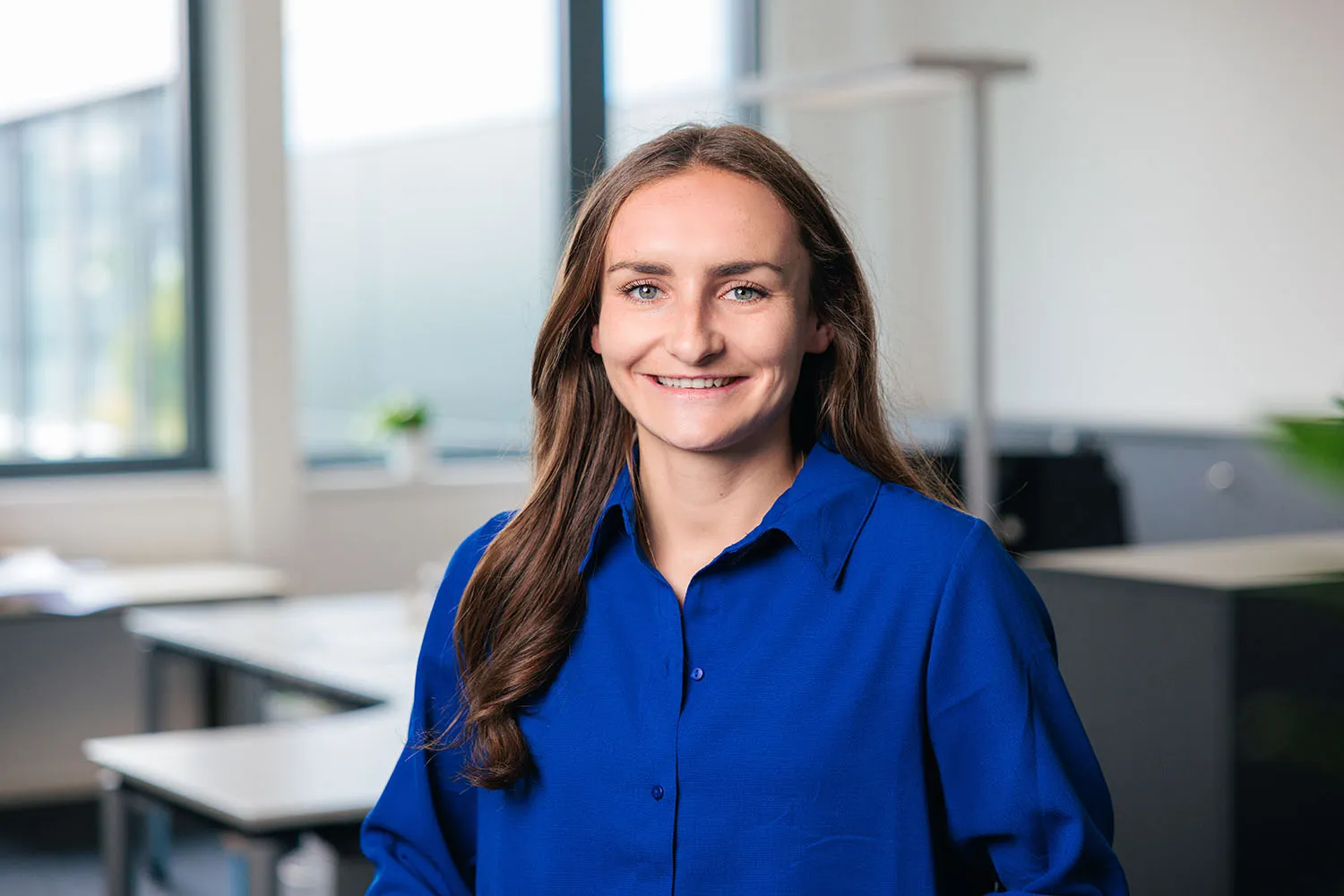 Porträt einer Frau mit langen dunklen Haaren und blauer Bluse im Büro.