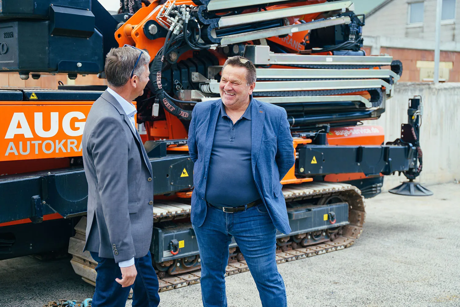 Zwei Männer stehen nebeneinander in einer Werkhalle mit Maschinen im Hintergrund.