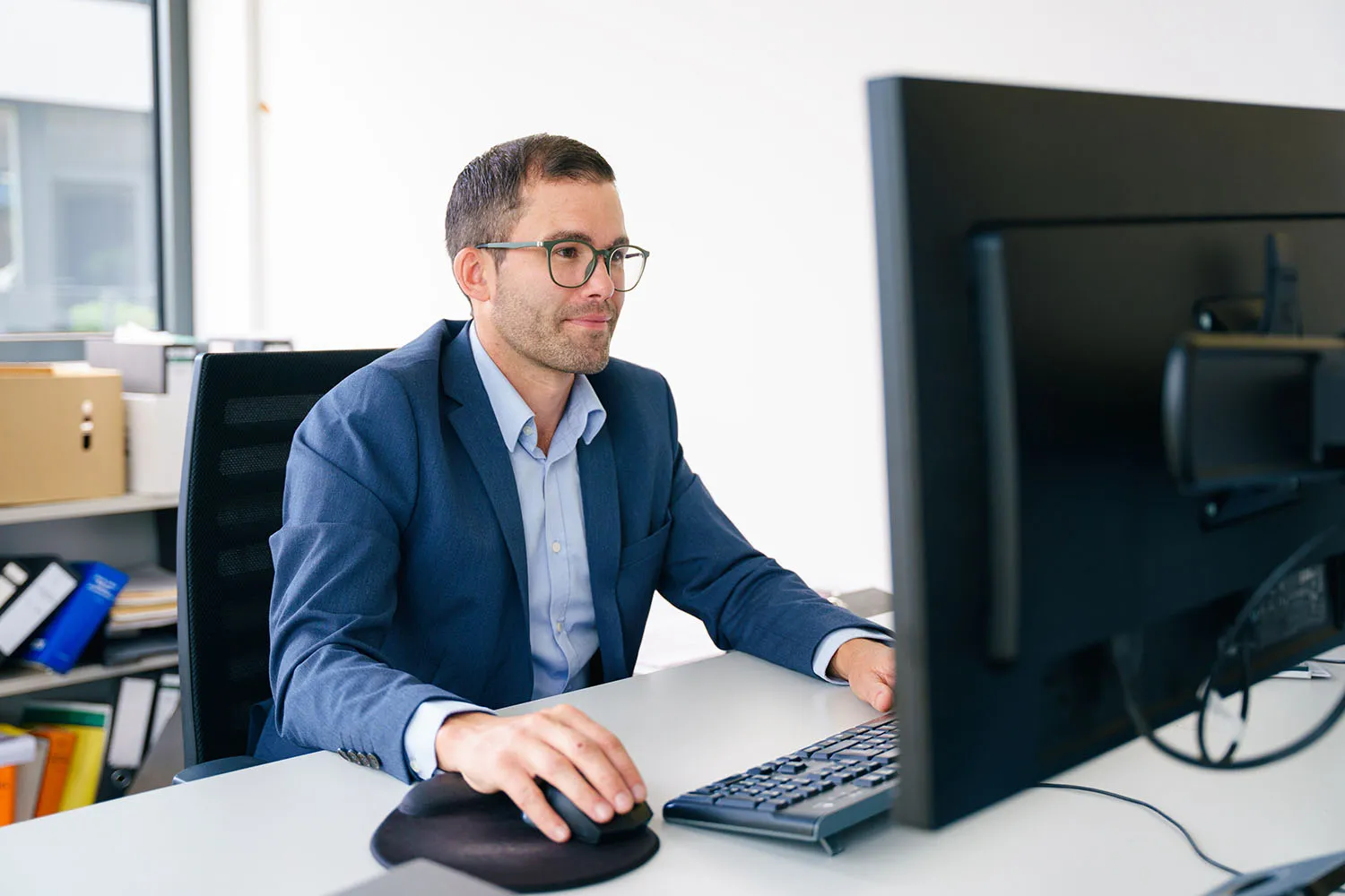Mann im Sakko arbeitet konzentriert an einem Desktop-PC im Büro.
