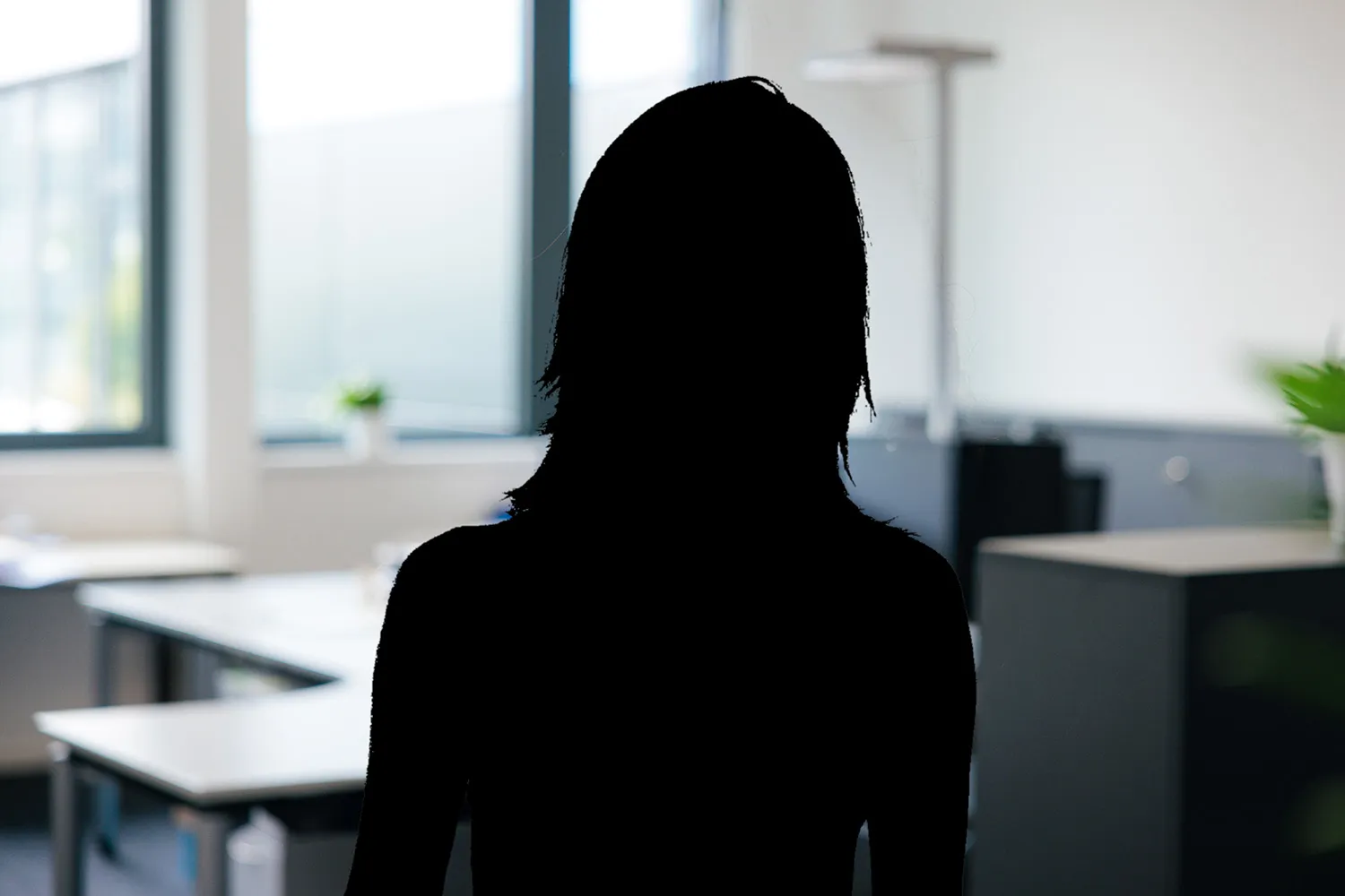 Silhouette einer Person vor einem hellen Büroarbeitsplatz, Person nicht erkennbar.