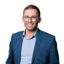 Porträt eines Mannes mit Brille, blauem Sakko und hellem Hemd.