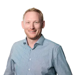 Porträt eines Mannes mit kurzem Haar, blauem Hemd und freundlichem Lächeln.