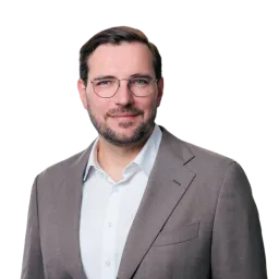 Porträt eines Mannes mit Bart, Brille und grauem Sakko.