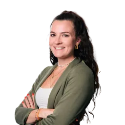 Porträt einer Frau mit dunklen Haaren, grünem Blazer und verschränkten Armen vor neutralem, dunklem Hintergrund.