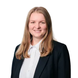 Porträt einer Frau mit langen blonden Haaren und schwarzem Blazer vor neutralem, dunklem Hintergrund.