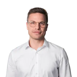 Porträt eines Mannes mit Brille, weißem Hemd und neutralem Gesichtsausdruck.