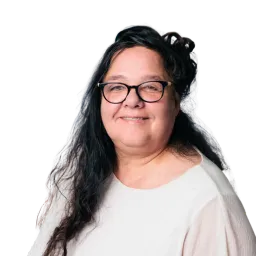 Porträt einer Frau mit dunklen Haaren, Brille und hellem Oberteil vor dunklem Hintergrund.