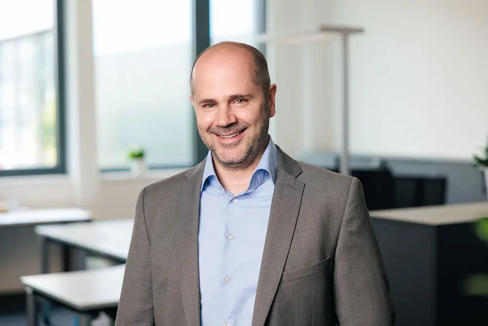 Lächelnder Mann in grauem Anzug und blauem Hemd in einem modernen Büro.