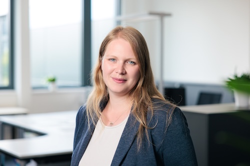 Porträt einer lächelnden blonden Frau in blauem Blazer in einem modernen Büro.