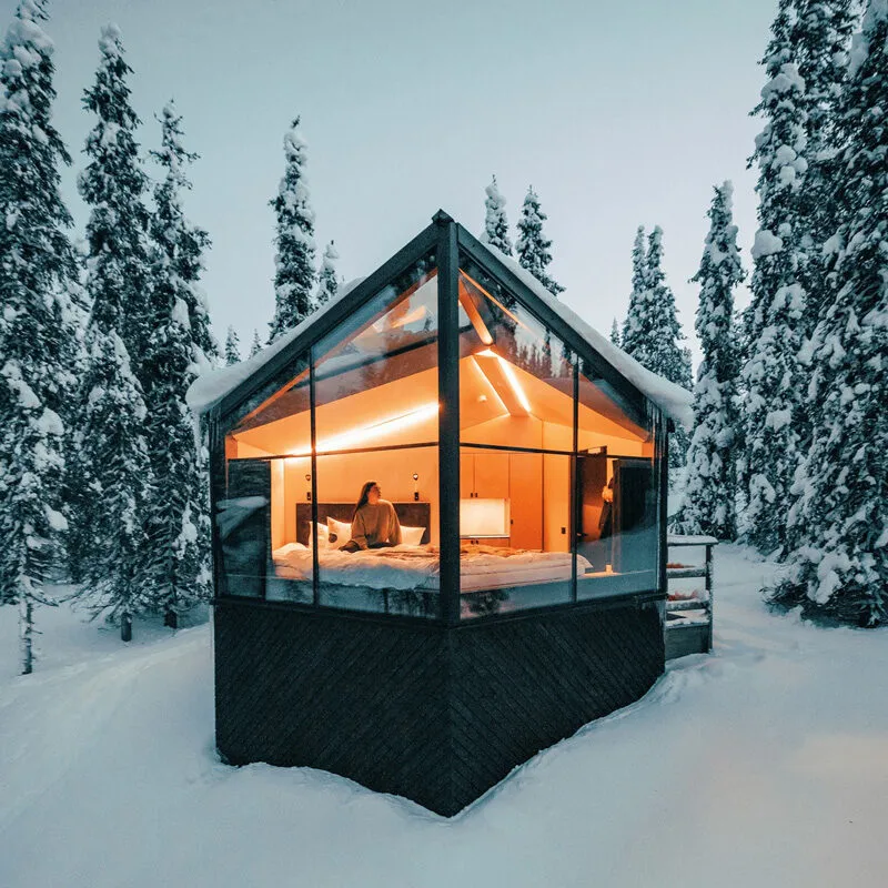 Vue extérieure d’un kota enneigé en Laponie pendant une expérience hivernale signée INÜI Collection.
