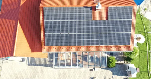 Hausdach mit großen Solarmodulen, Wintergarten darunter.