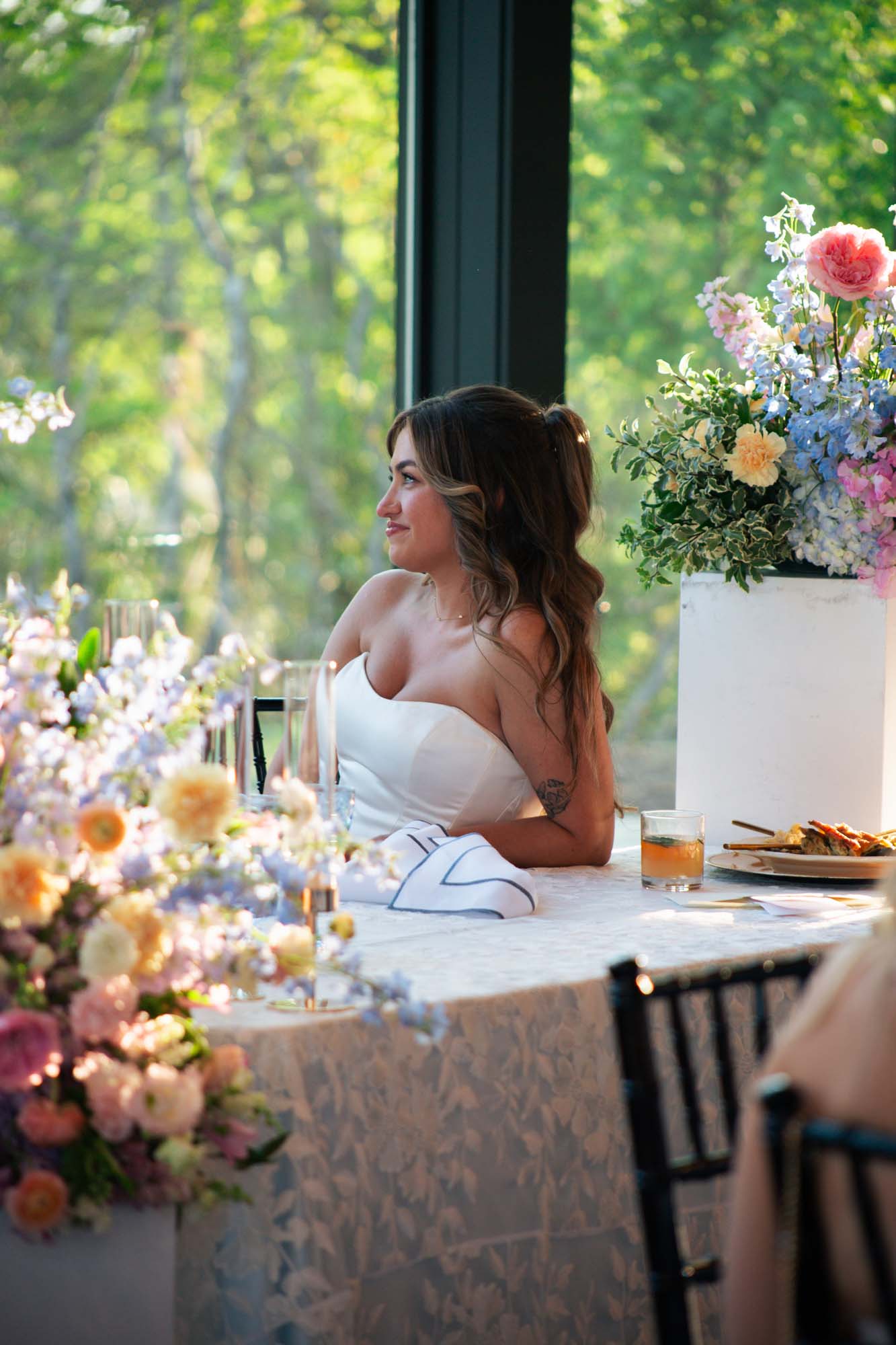 Woman watches view from a venue table with floral arrangements.