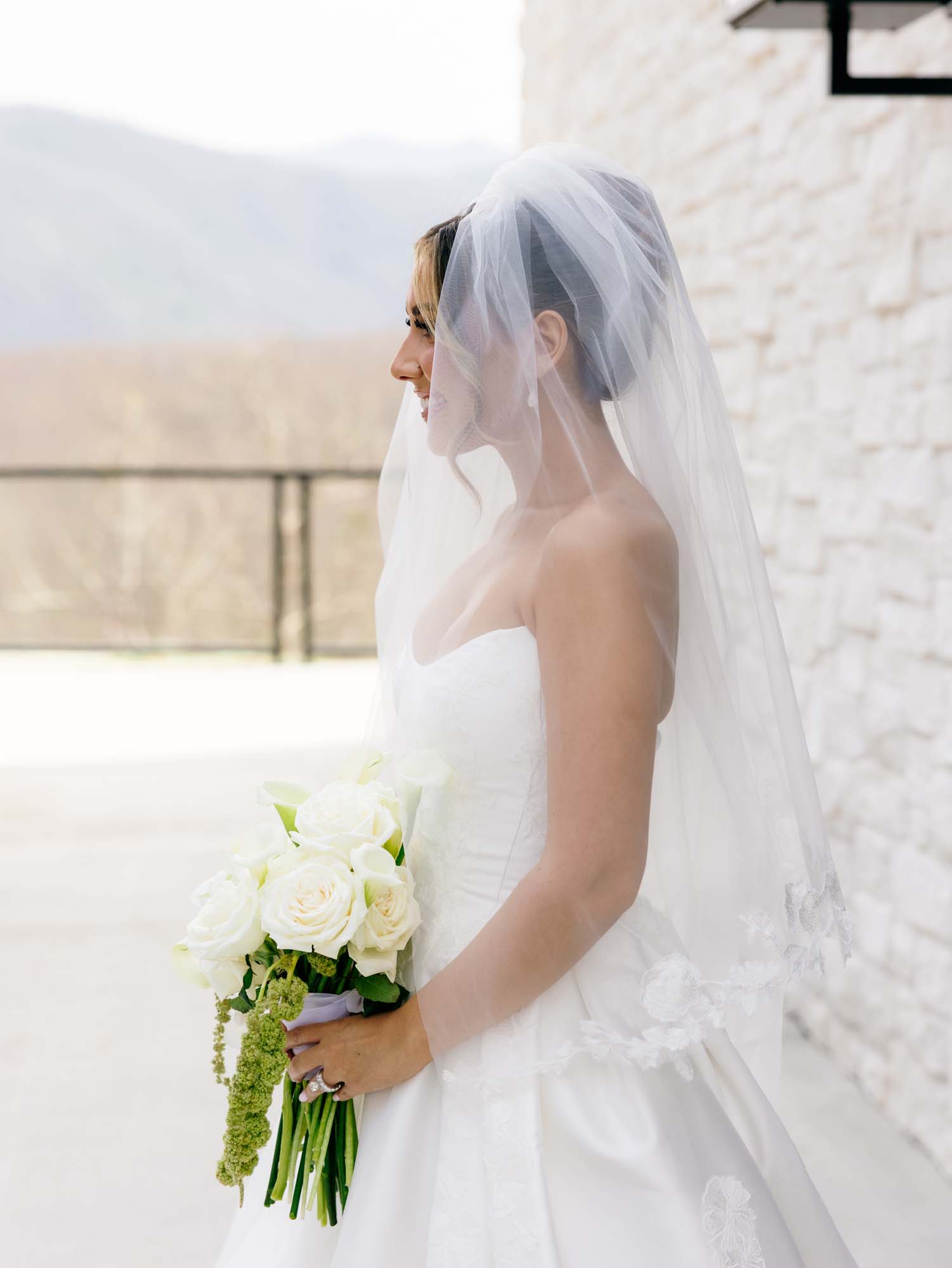 Bride in veil holds white bouquet outdoors at a wedding venue.