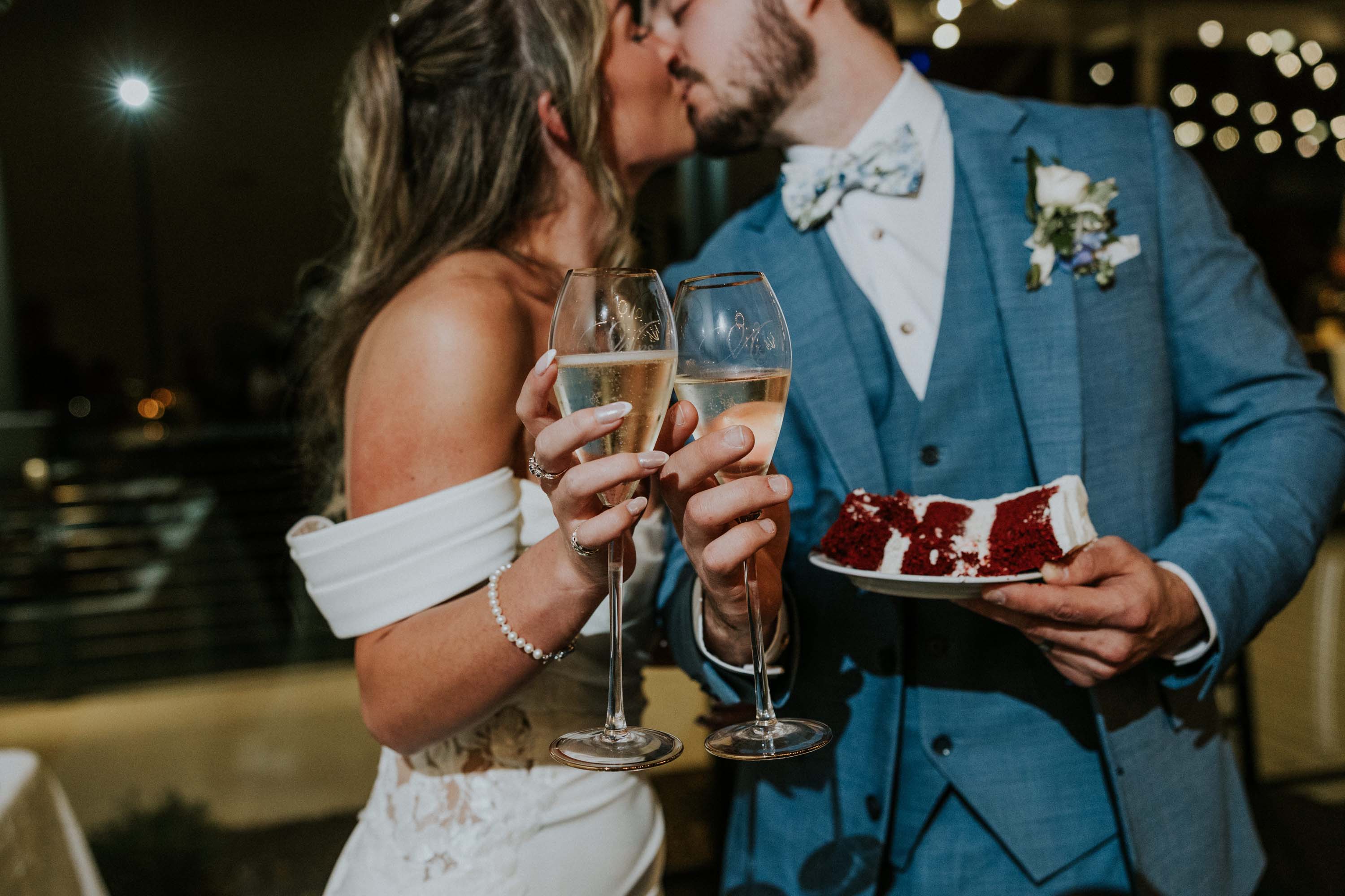 Couple kissing, toasting with champagne while holding a dessert at Trailhead Venues.
