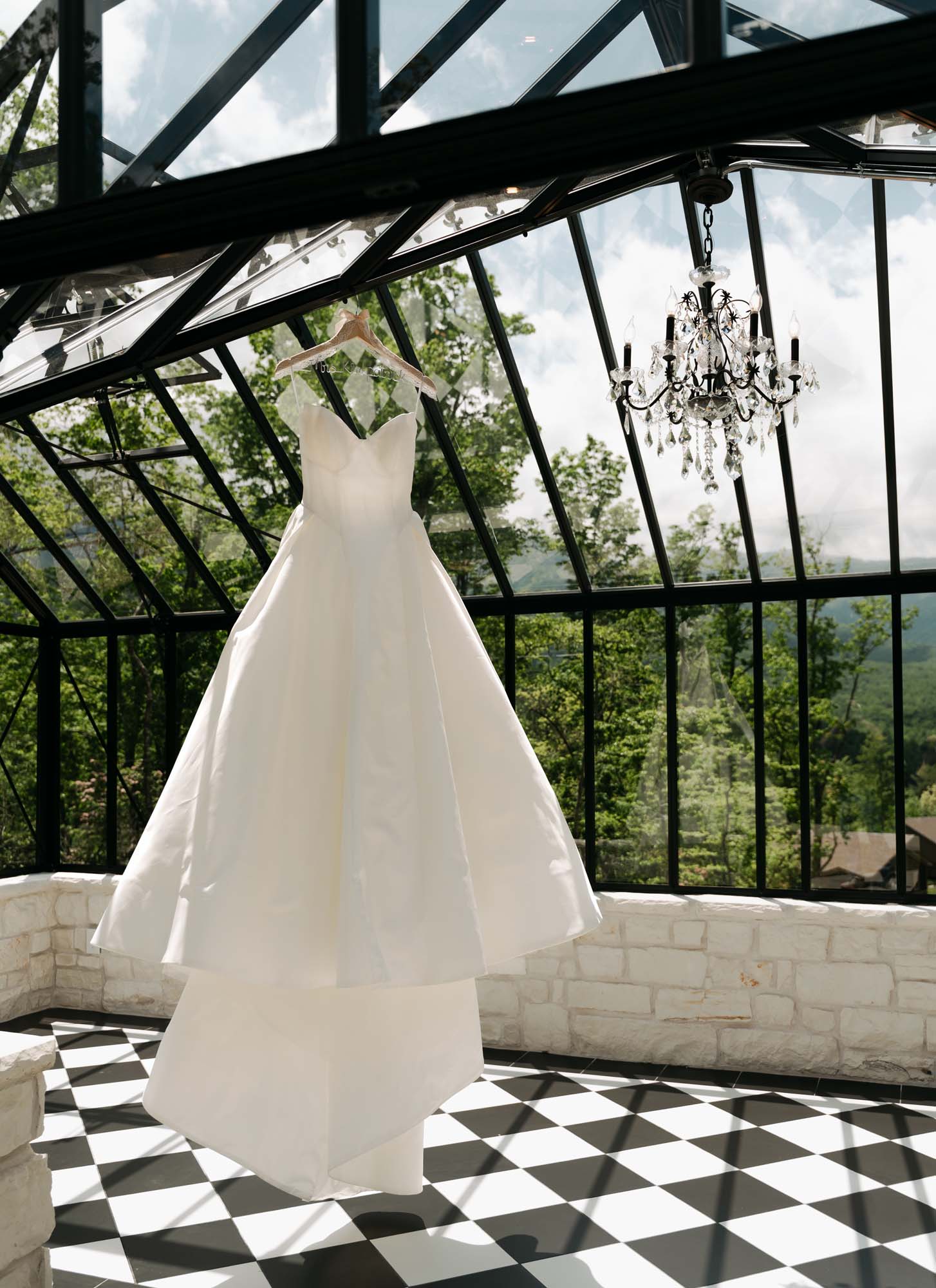 White wedding dress displayed in a glass-enclosed venue overlooking mountains.