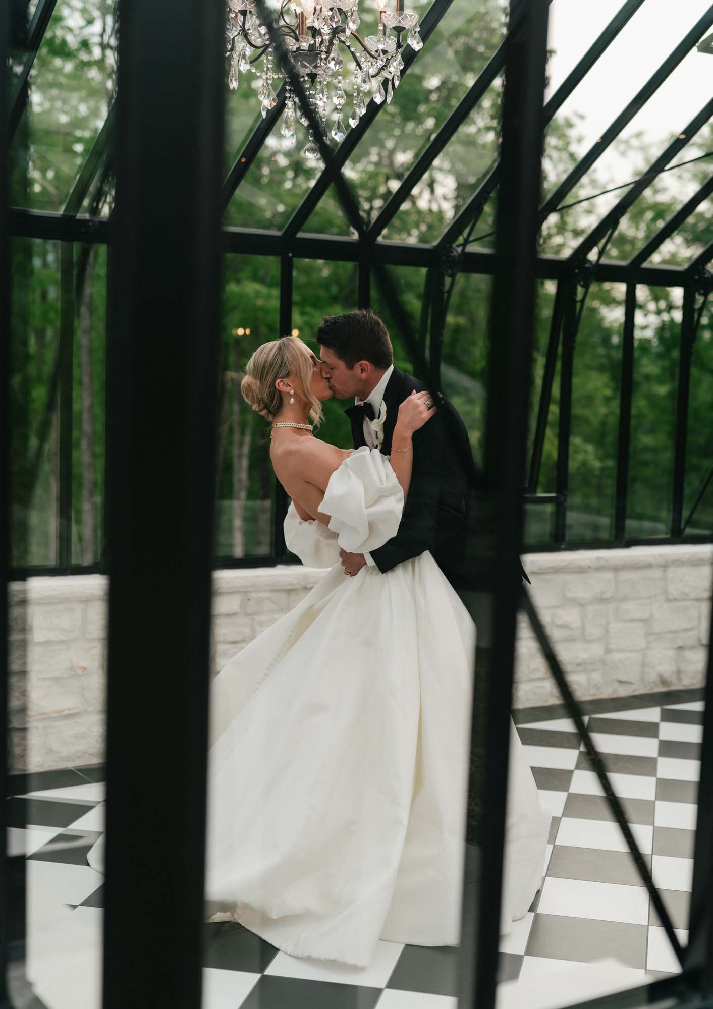 Newlyweds embrace under a glass structure at Trailhead Venues.