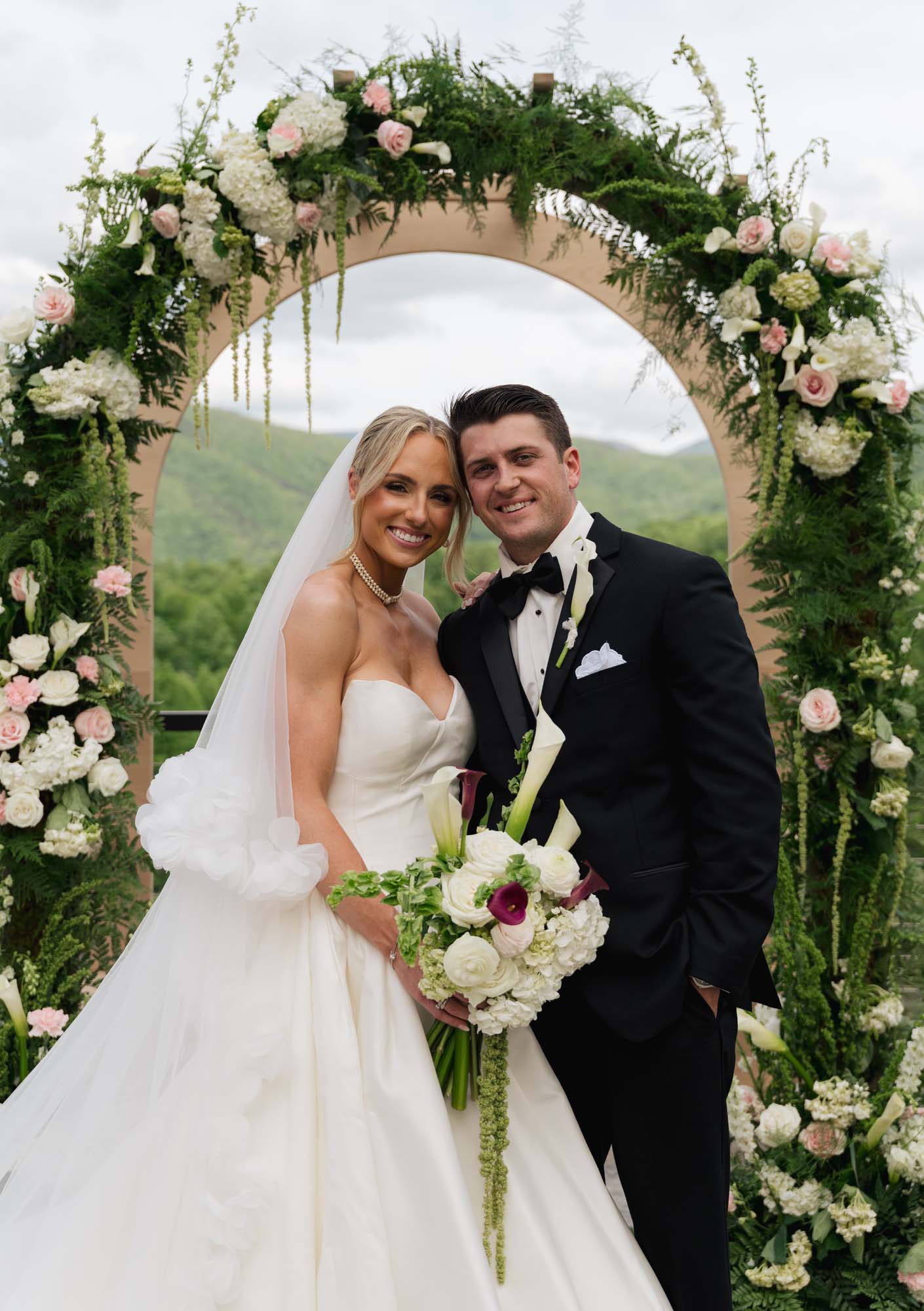 Newly married couple stands beneath a floral arch at Trailhead Venues.