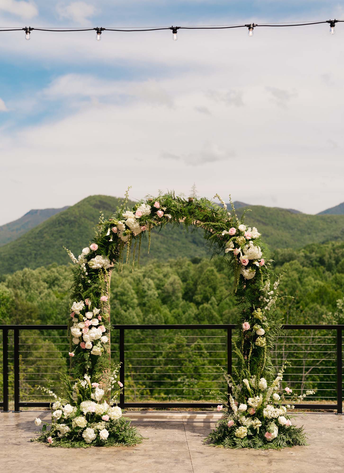 Floral archway setup at a mountain wedding venue overlooking trees.