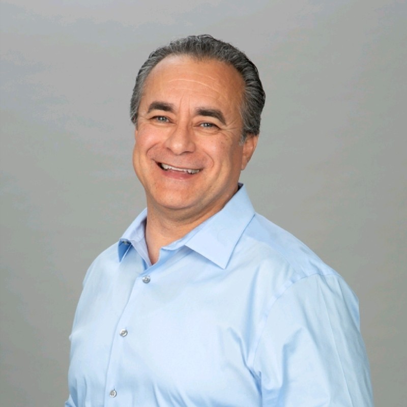 Middle-aged man in light blue shirt smiling warmly at camera