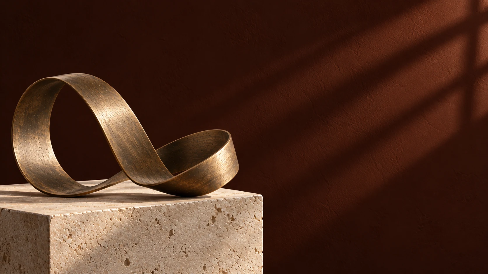 Bronze ribbon sculpture on a stone plinth against a warm, shadowed wall