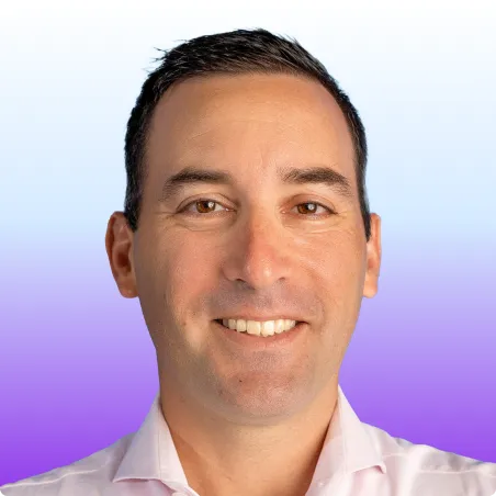 Man with short dark hair wearing a light pink shirt against a purple gradient background.