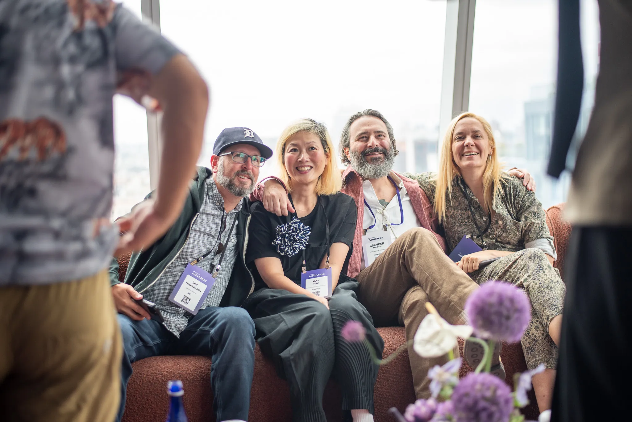 Four people sitting closely on a couch smiling, two standing people partially framing the photo.