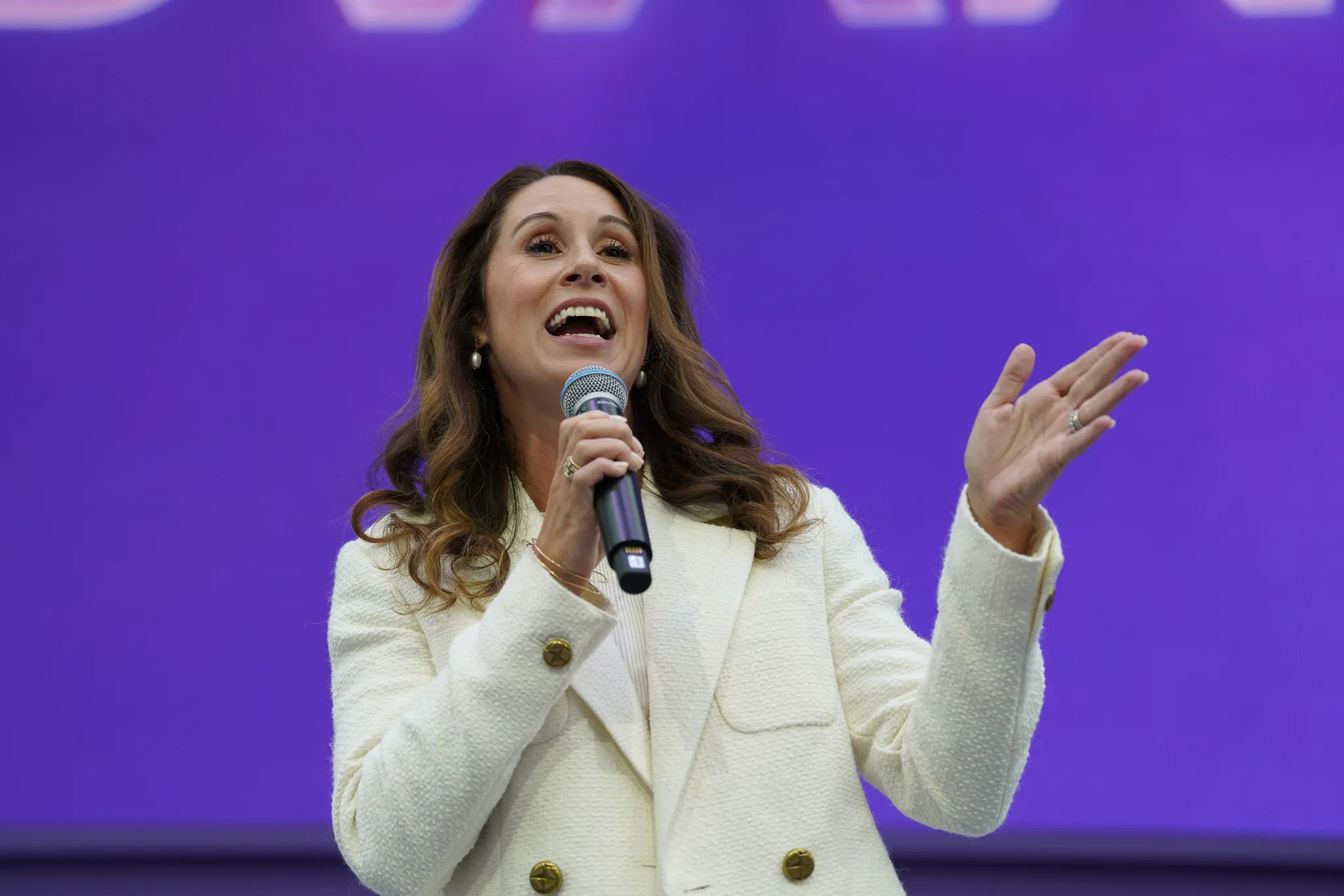 Woman wearing striped jacket and speaking enthusiastically from a seated position on stage.