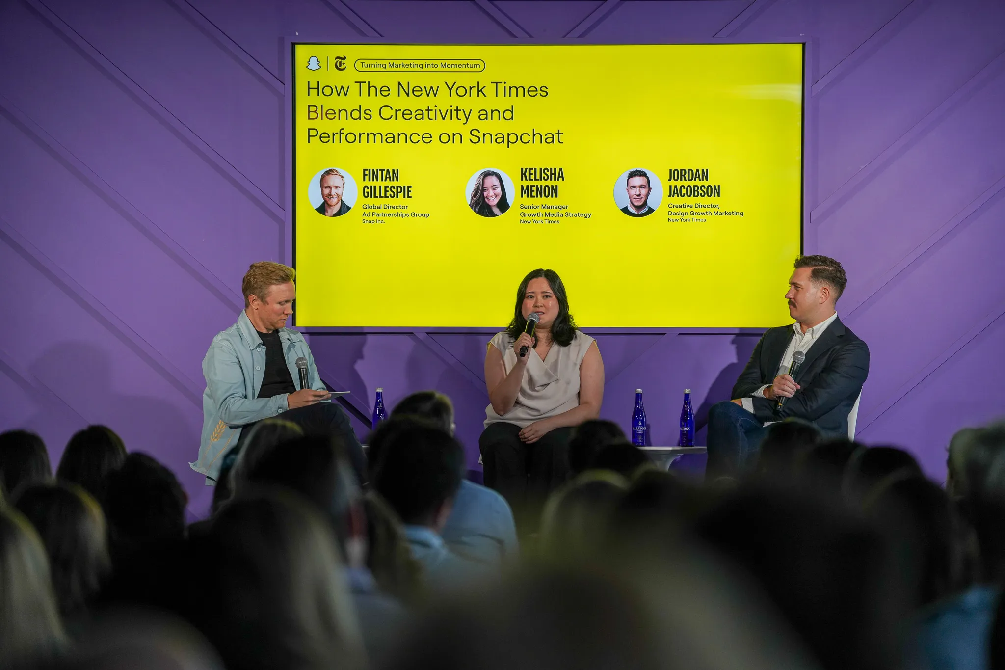 Woman with microphone speaking animatedly during a panel discussion with purple background.