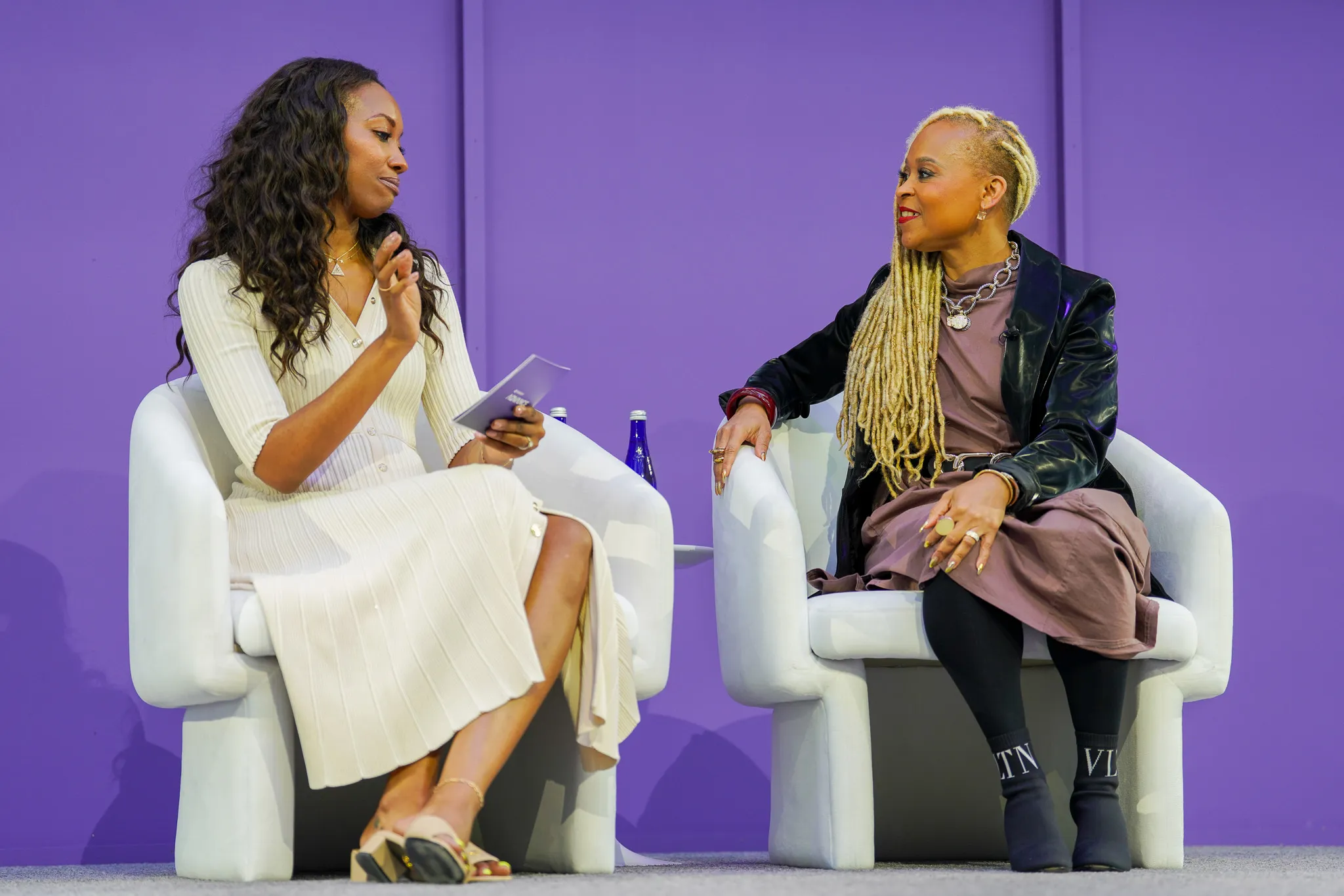 Two men smiling and holding microphones while seated on stage at an event.