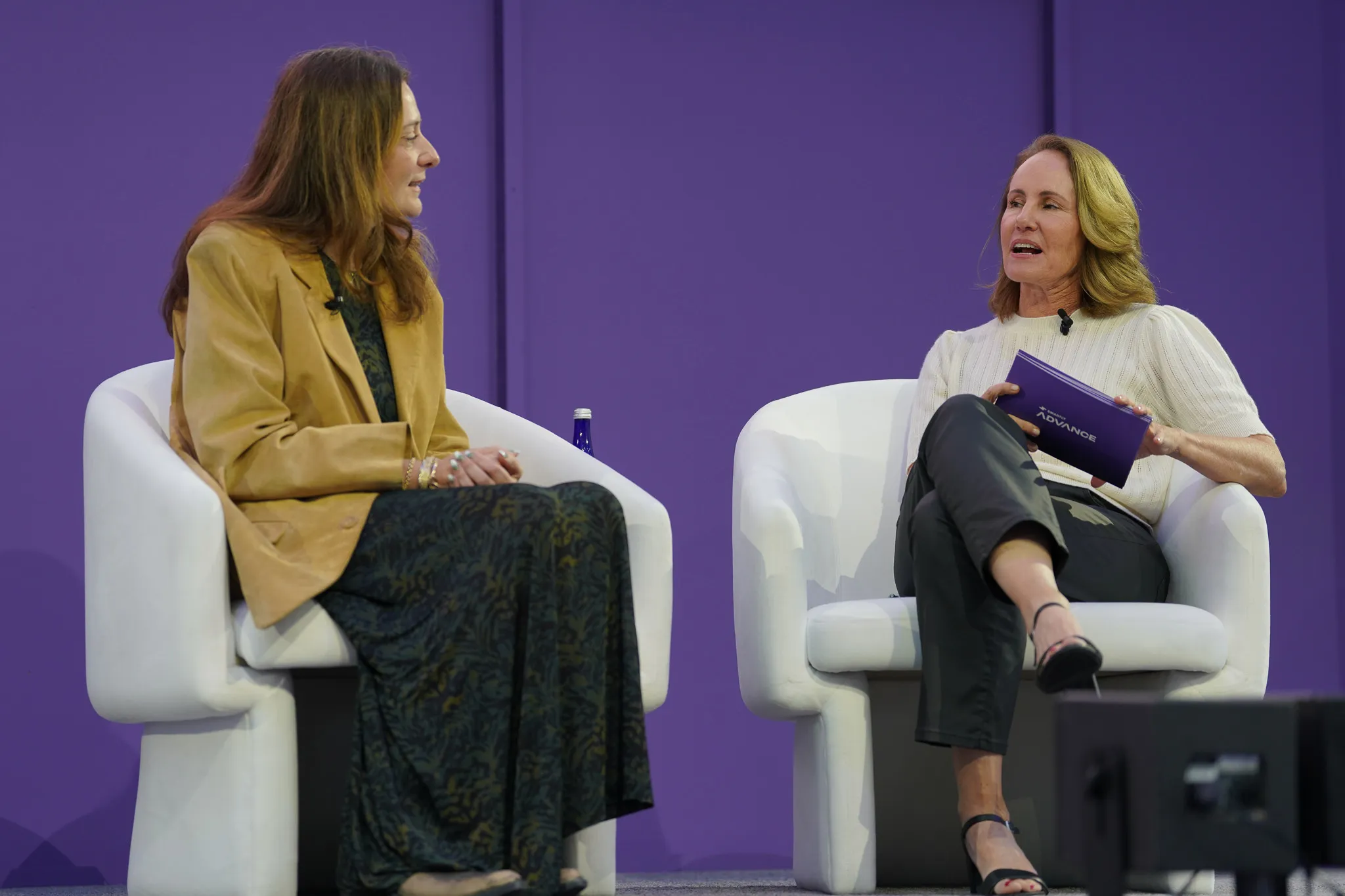 Two women seated, smiling and talking during a panel discussion on stage.