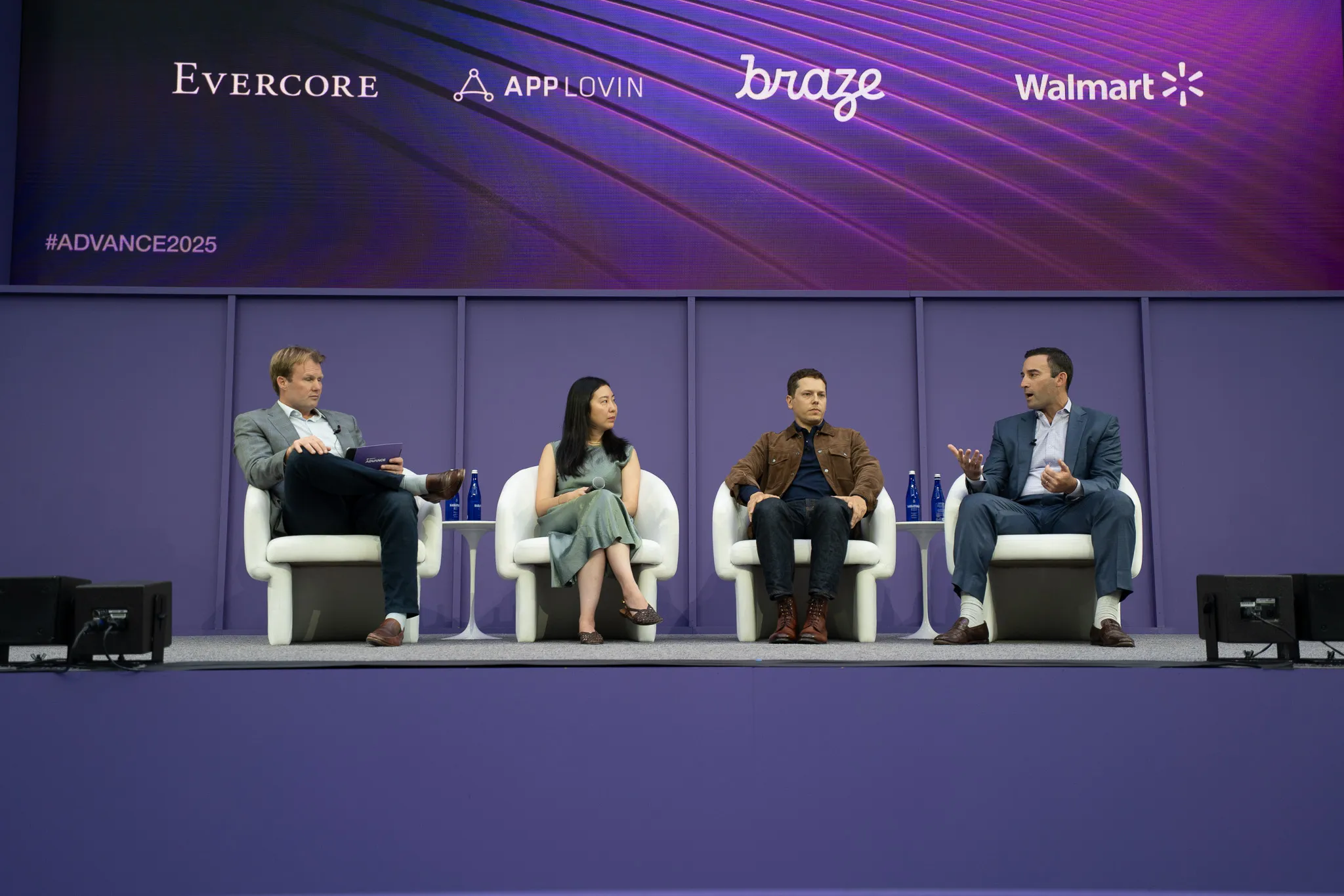 Four panelists engaged in conversation on stage with purple curtain backdrop at a conference.