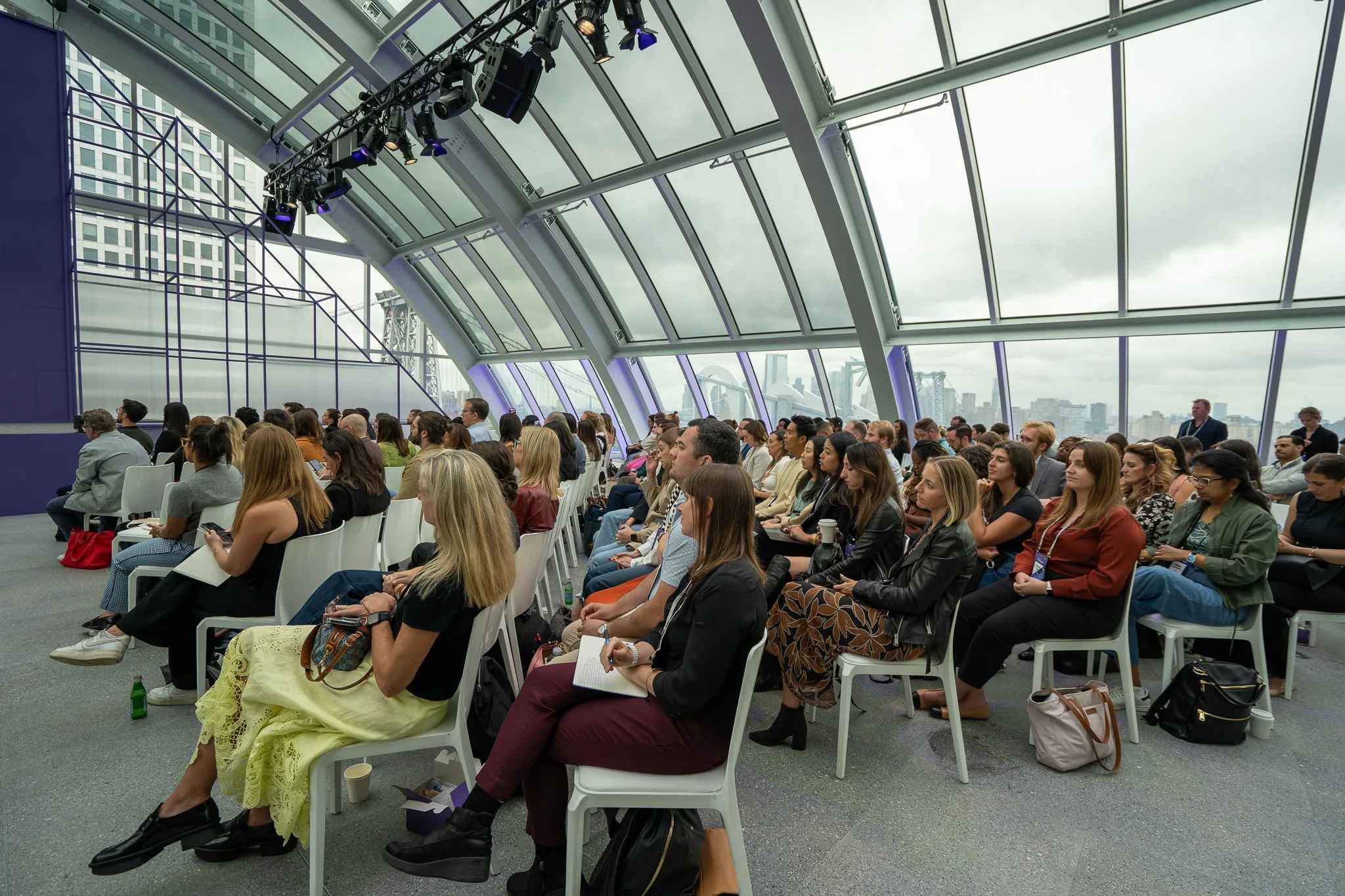 People socializing and working at tables in a purple-themed event space with neon lighting and plants.