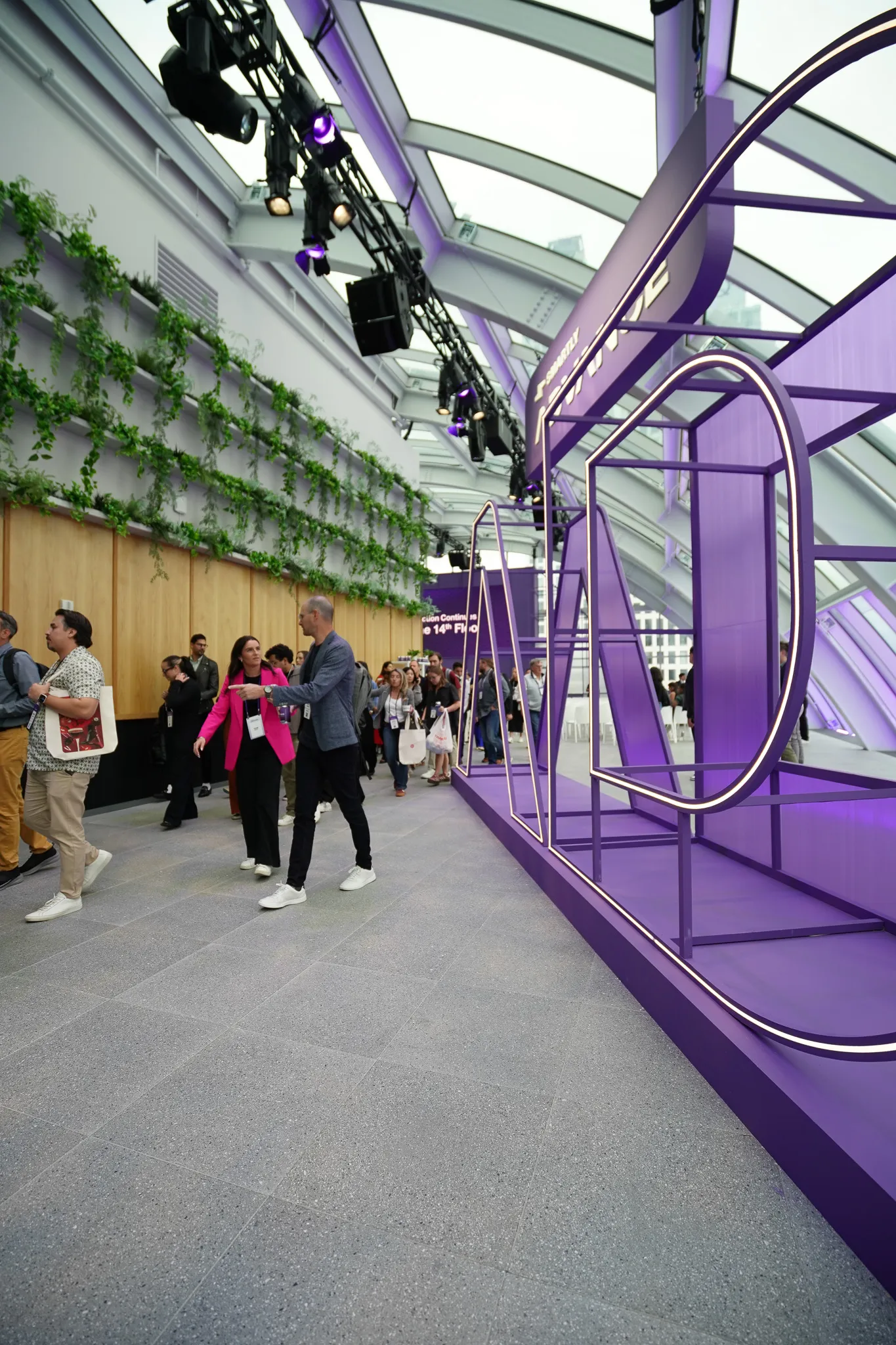 People walking near large purple letters spelling "ADVANCE" inside an indoor event space.