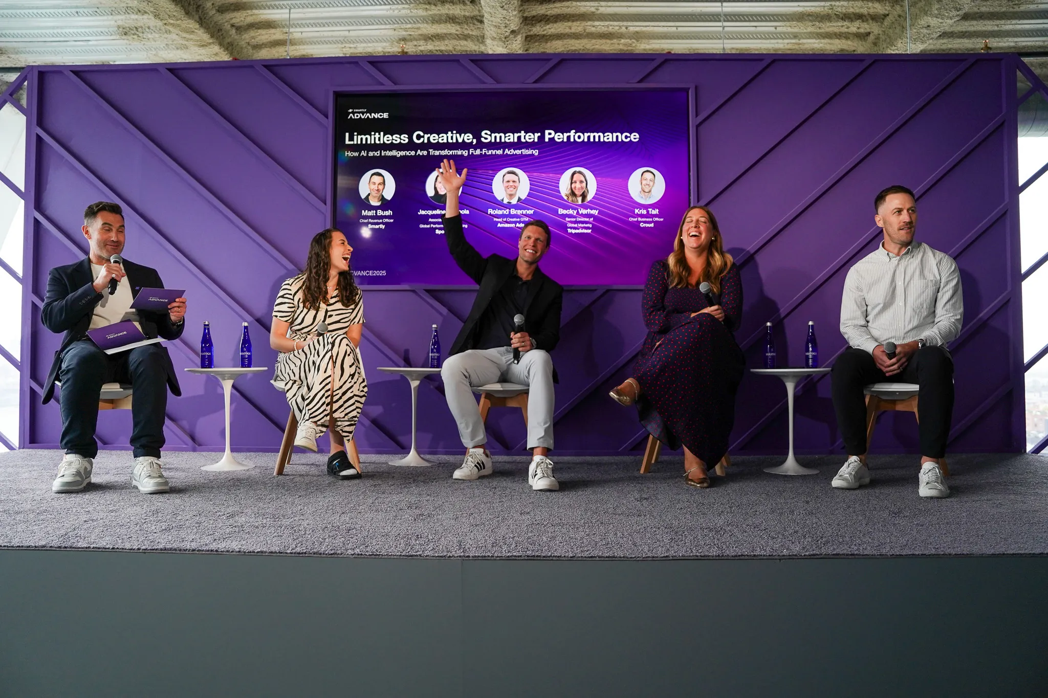 Five panelists sitting on chairs in front of a purple backdrop with presentation screen showing "Limitless Creative, Smarter Performance."