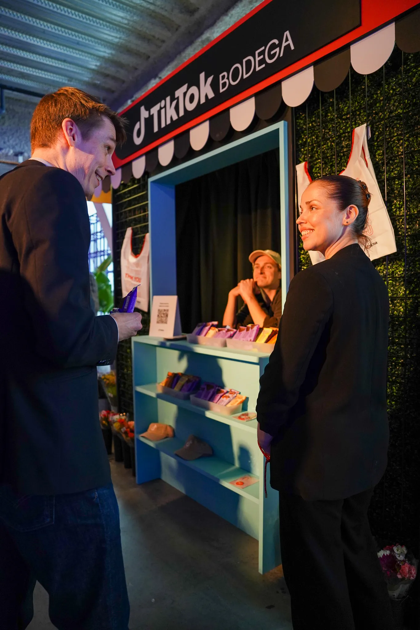 Crowd attending a conference with attendees seated facing a speaker stage inside a large event space with tall windows.