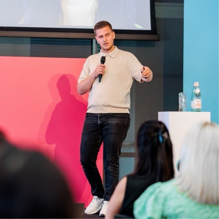Man holding a microphone and pointing while speaking to an audience in a conference room.
