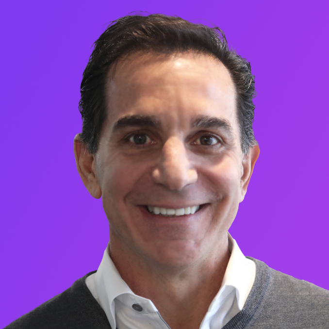 Smiling middle-aged man with dark hair wearing a white shirt and gray sweater against purple background.