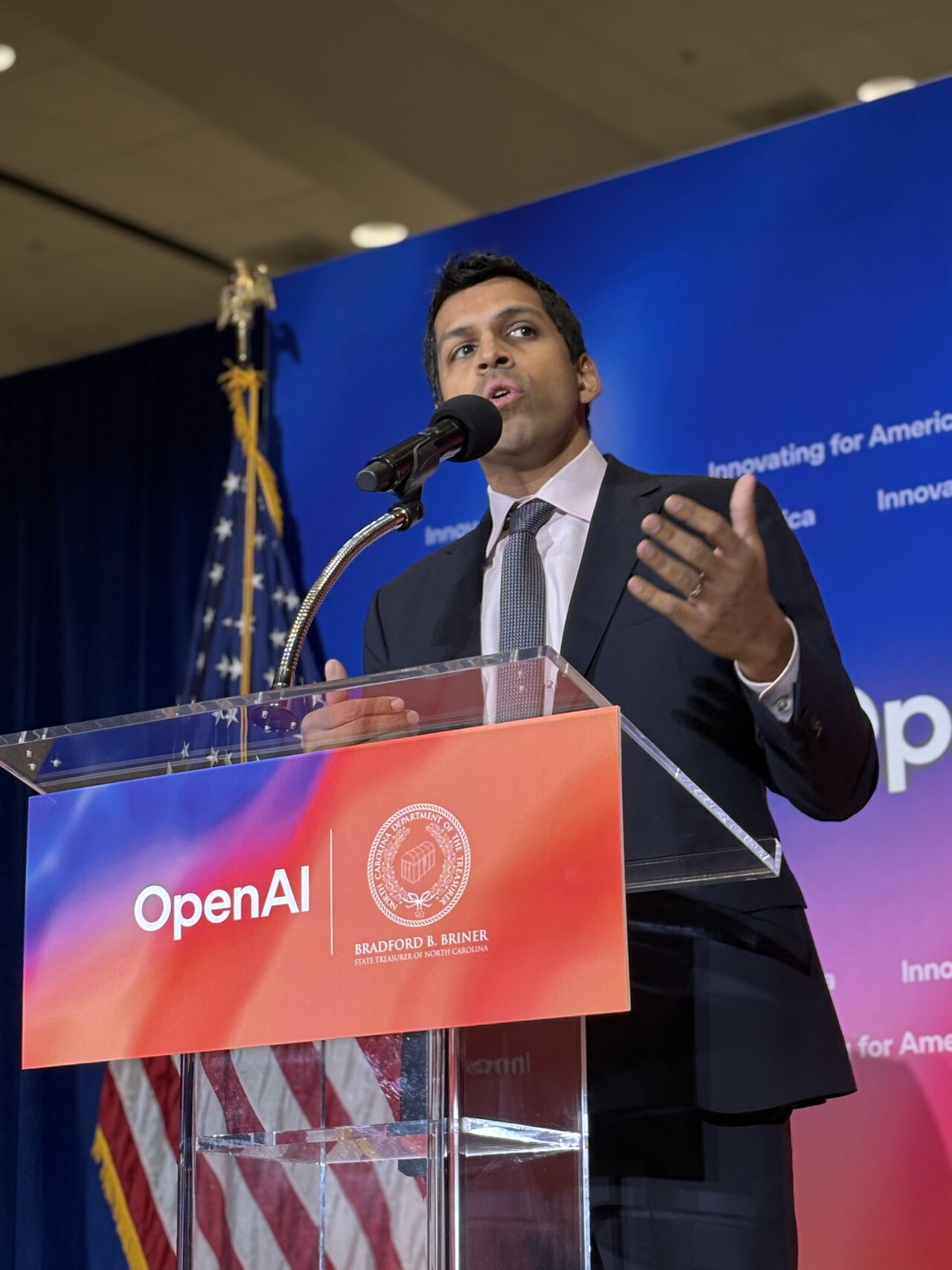 Ronnie giving a speech behind an OpenAI podium 