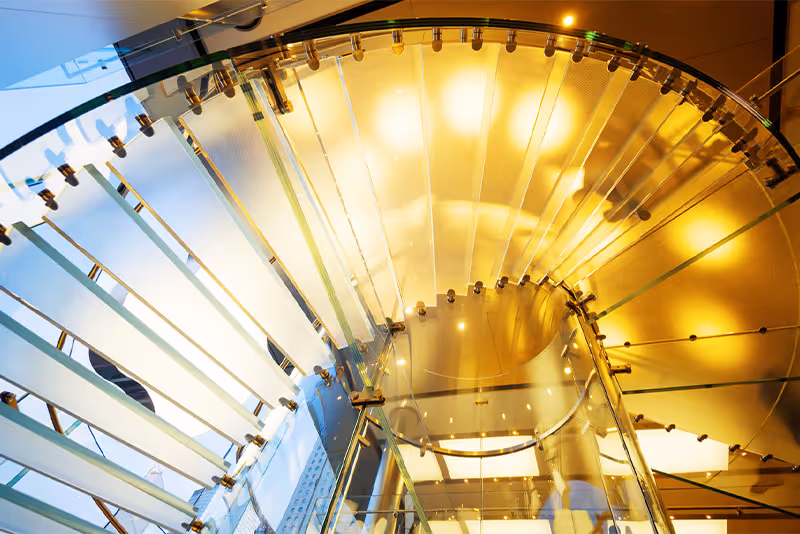 Elegant spiral glass staircase with warm golden lighting and metal supports