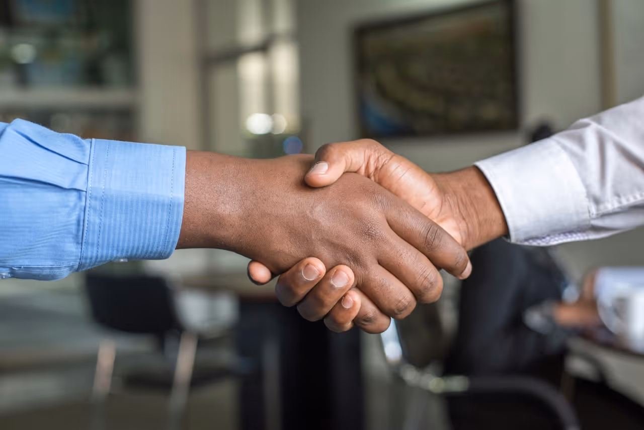 Close-up of two people shaking hands, one wearing a blue shirt and the other a white shirt.