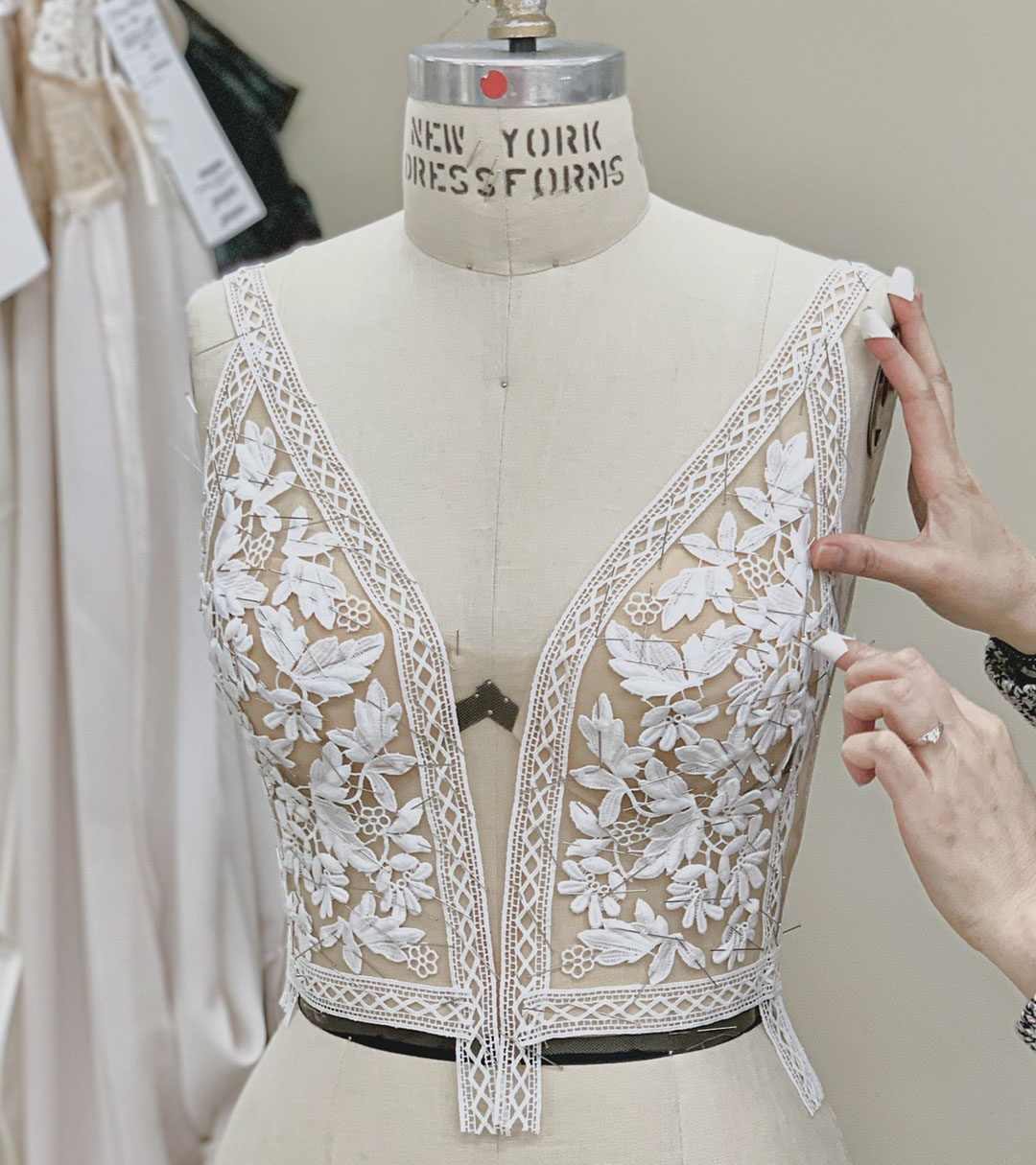 Sheer deep-V wedding bodice on a dress form featuring embroidered floral lace appliqués and delicate trim detailing.