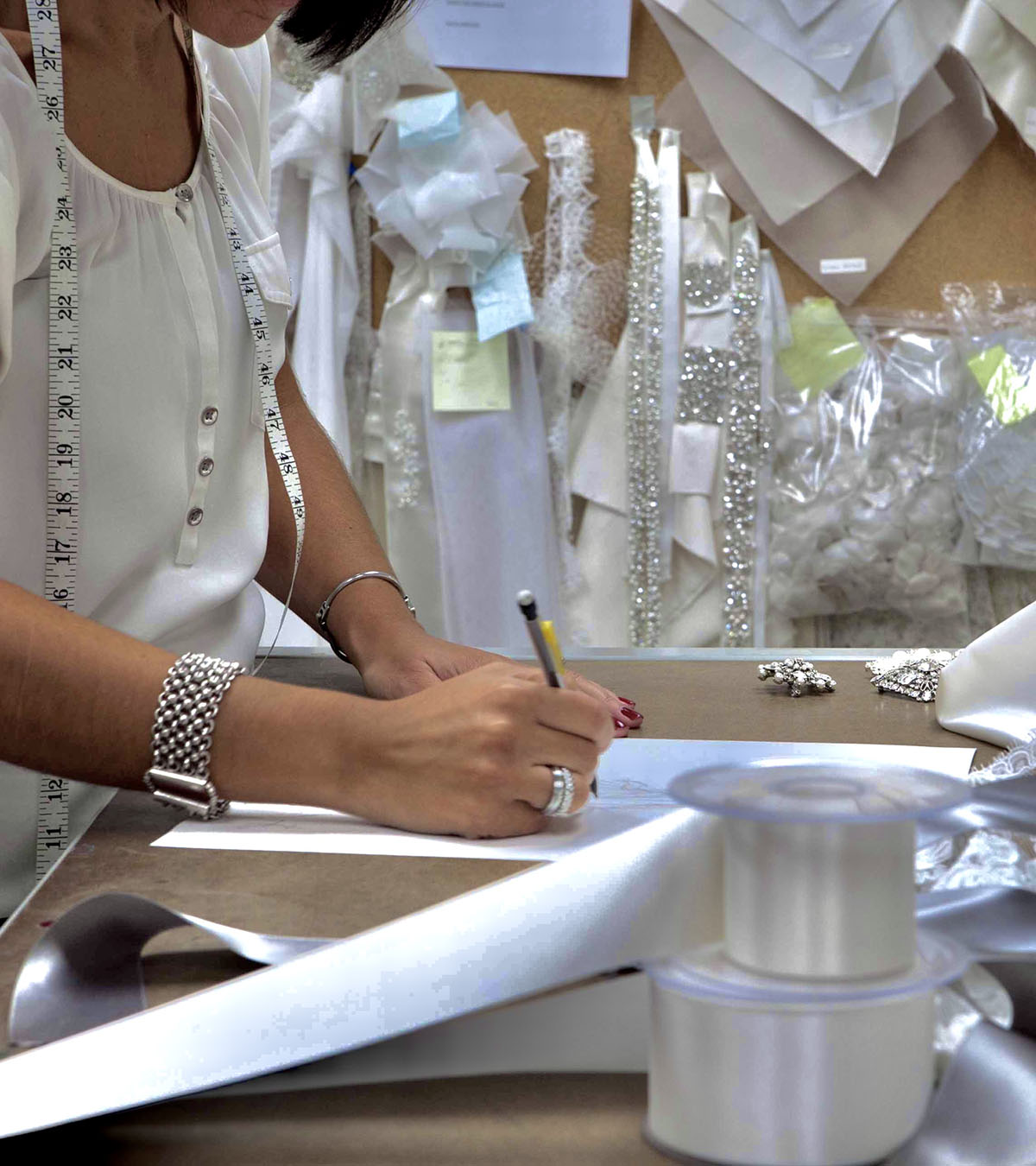Designer working on wedding dress patterns with fabric and embellishments in bridal atelier workspace.
