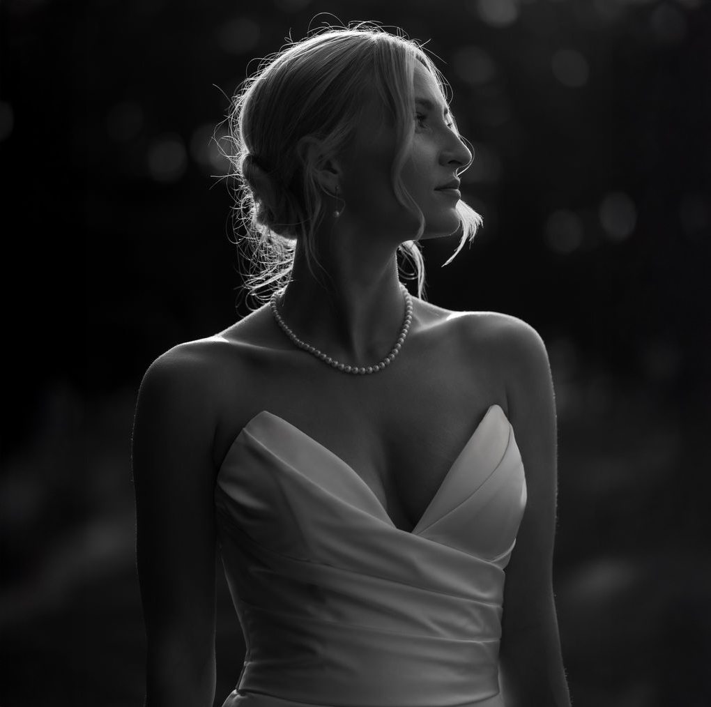 Black and white portrait of a bride in a strapless dress and pearl necklace looking to the side with hair in an updo.