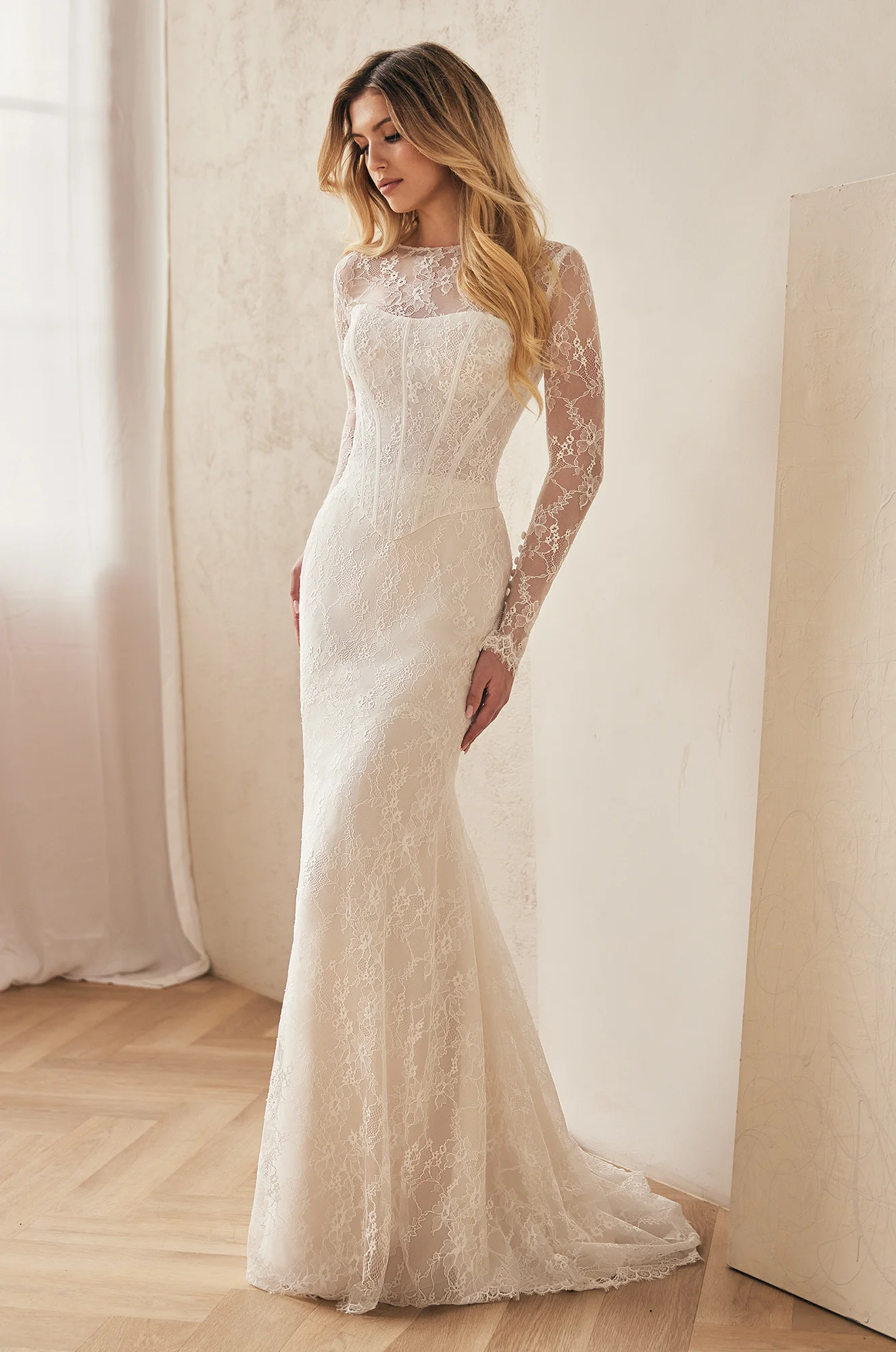 Front view of lace wedding dress with long sleeves, corset bodice, and fit and flare lace skirt, in a ballroom.