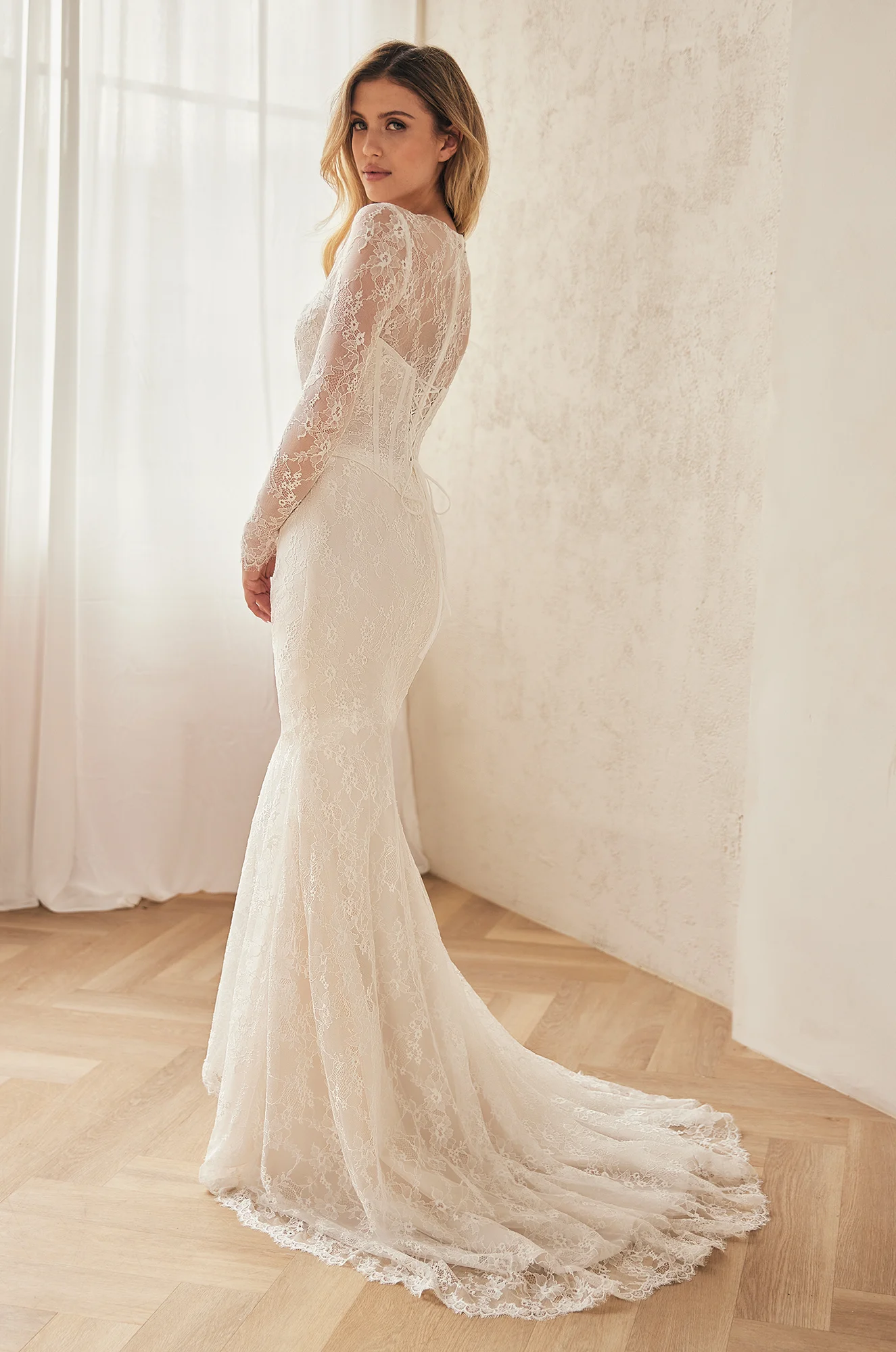 Back view of lace wedding dress with long sleeves, corset bodice with lace-up back, and fit and flare lace skirt, in a ballroom.