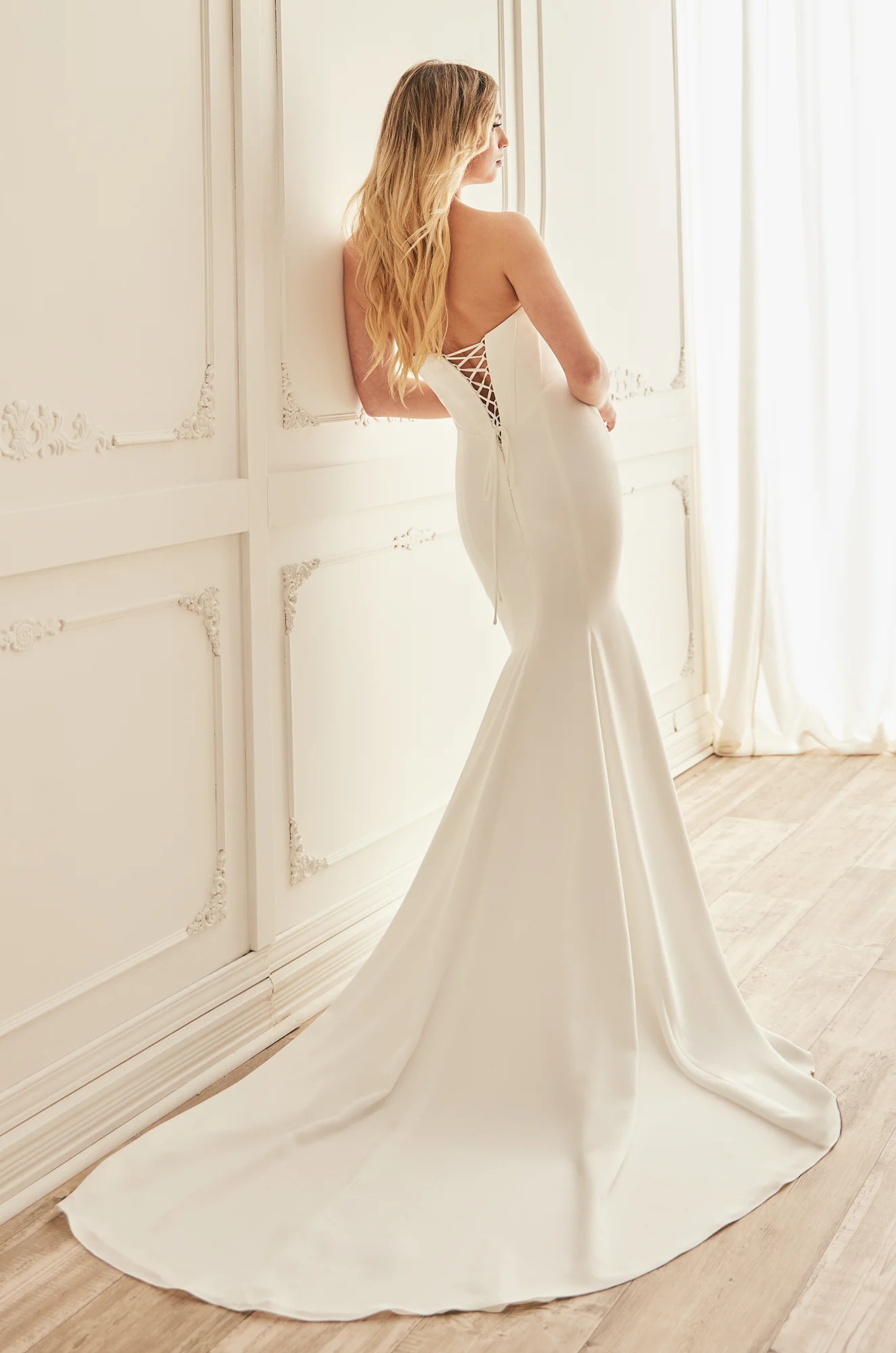 Back view of strapless Crepe wedding dress with corset lace-up back and a fit and flare skirt, in a ballroom.