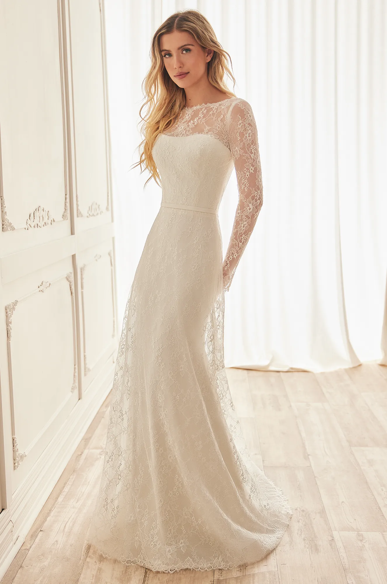 Front view of a strapless Crepe wedding dress with lace overlay that has long sleeves and a bateau neckline, with A-line lace overlay over fit and flare Crepe skirt, in a ballroom.